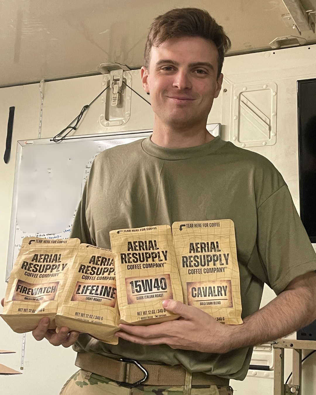 A soldier holding bags of Firewatch, Lifeline, 15W40 and Cavalry coffee from Aerial Resupply Coffee