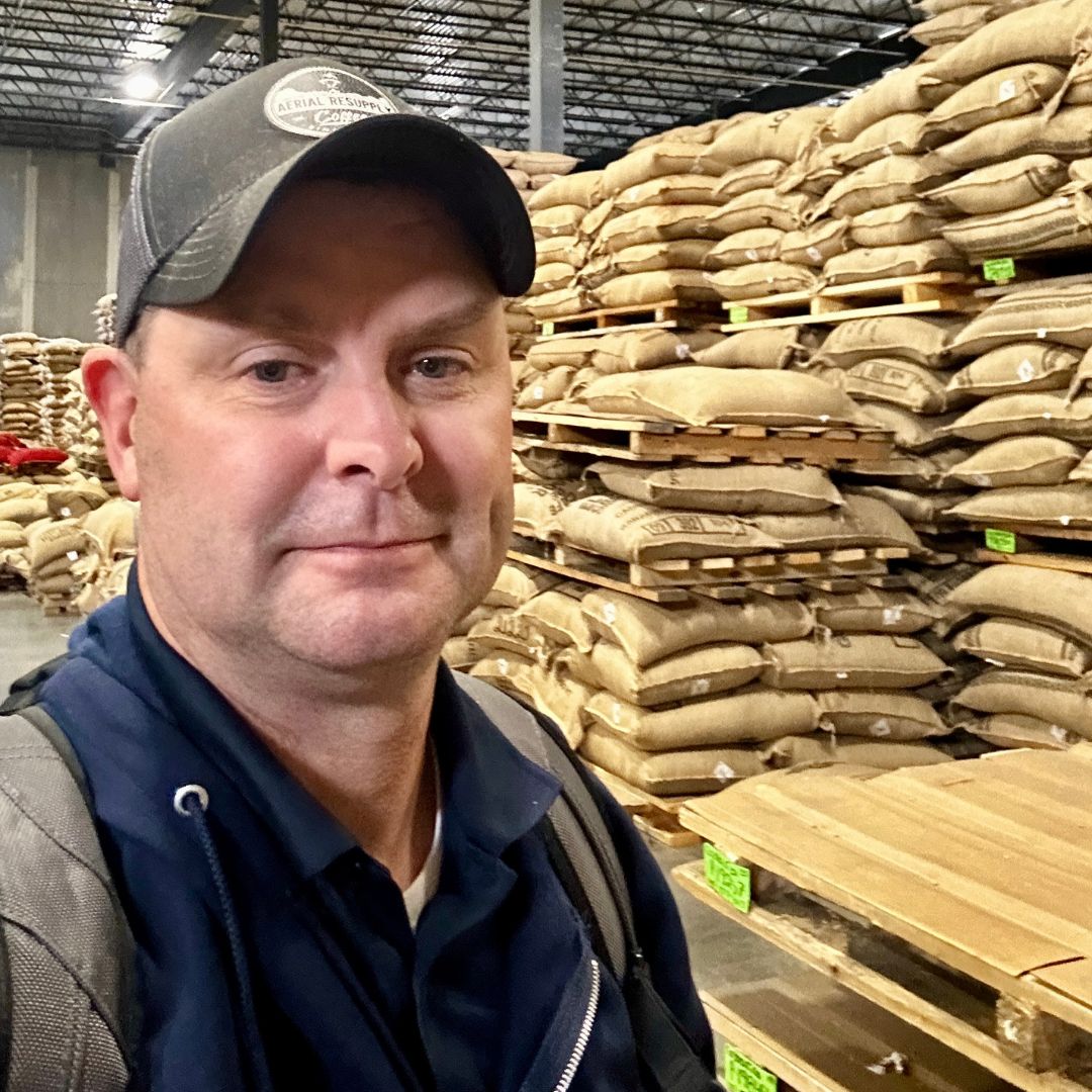Mike Klemmer among stacked bags of green coffee at the Cafe Imports warehouse