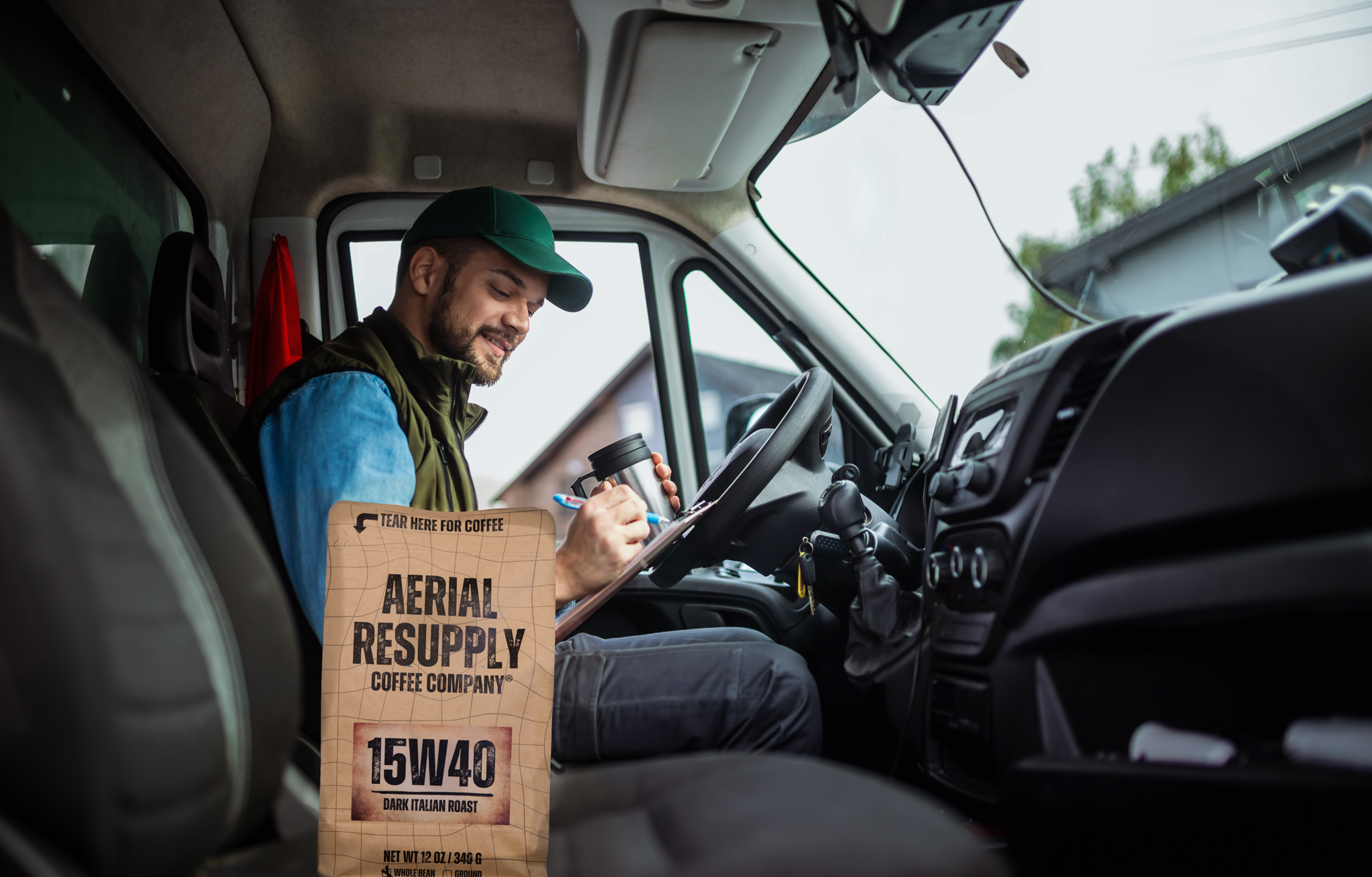 A truck driver holding a mug of Aerial Resupply Coffee 15W40 Dark Italian roast with a coffee bag as a display