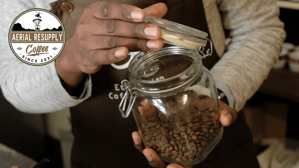 Whole bean coffee in a clear glass jar for storage held by a barista. Aerial Resupply Coffee. 