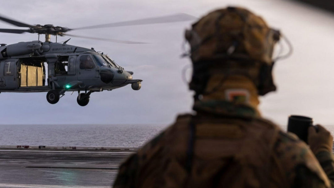 A Soldier holding a cup of coffee watching a helicopter land