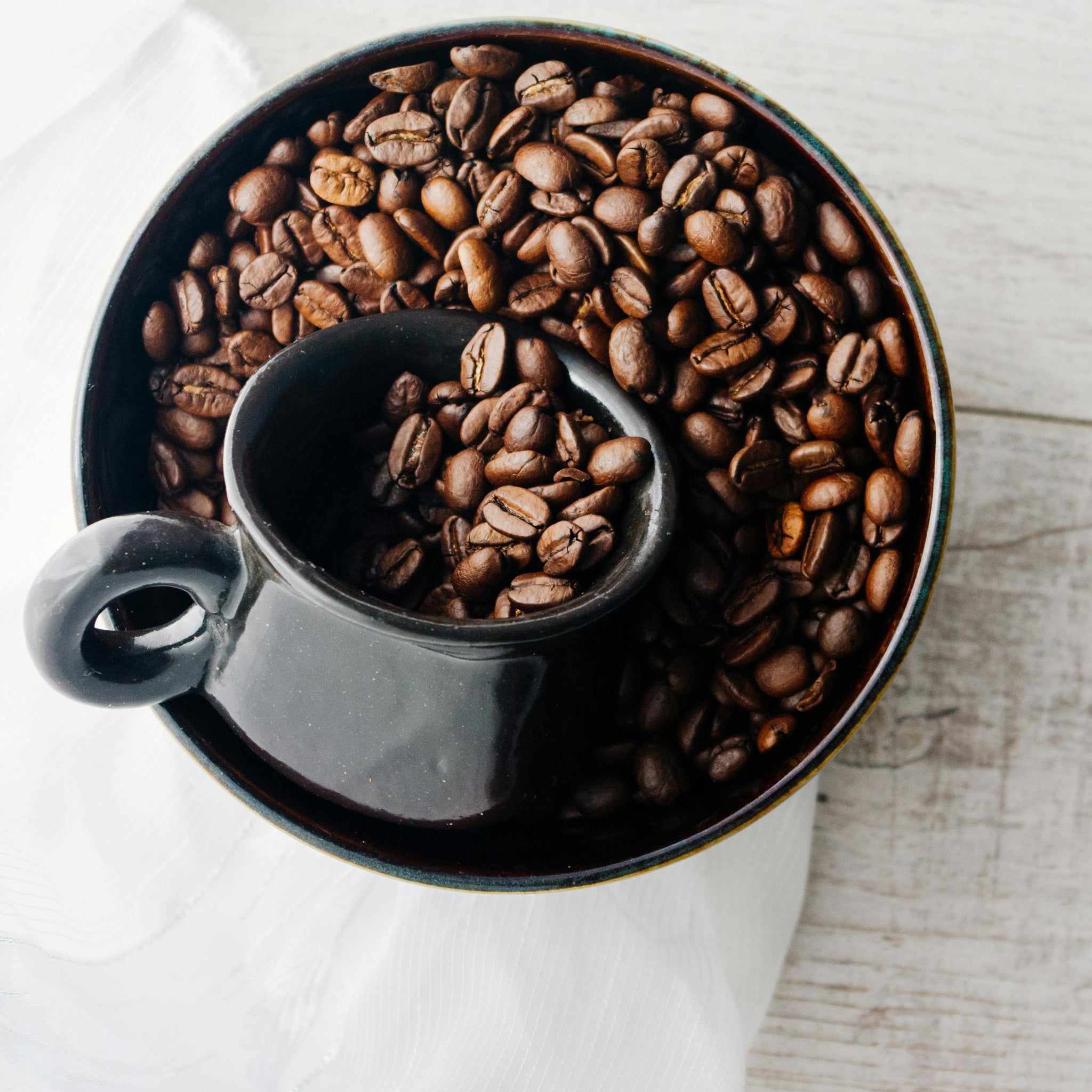 Coffee ice cream in a white bowl next to a spoon and coffee beans