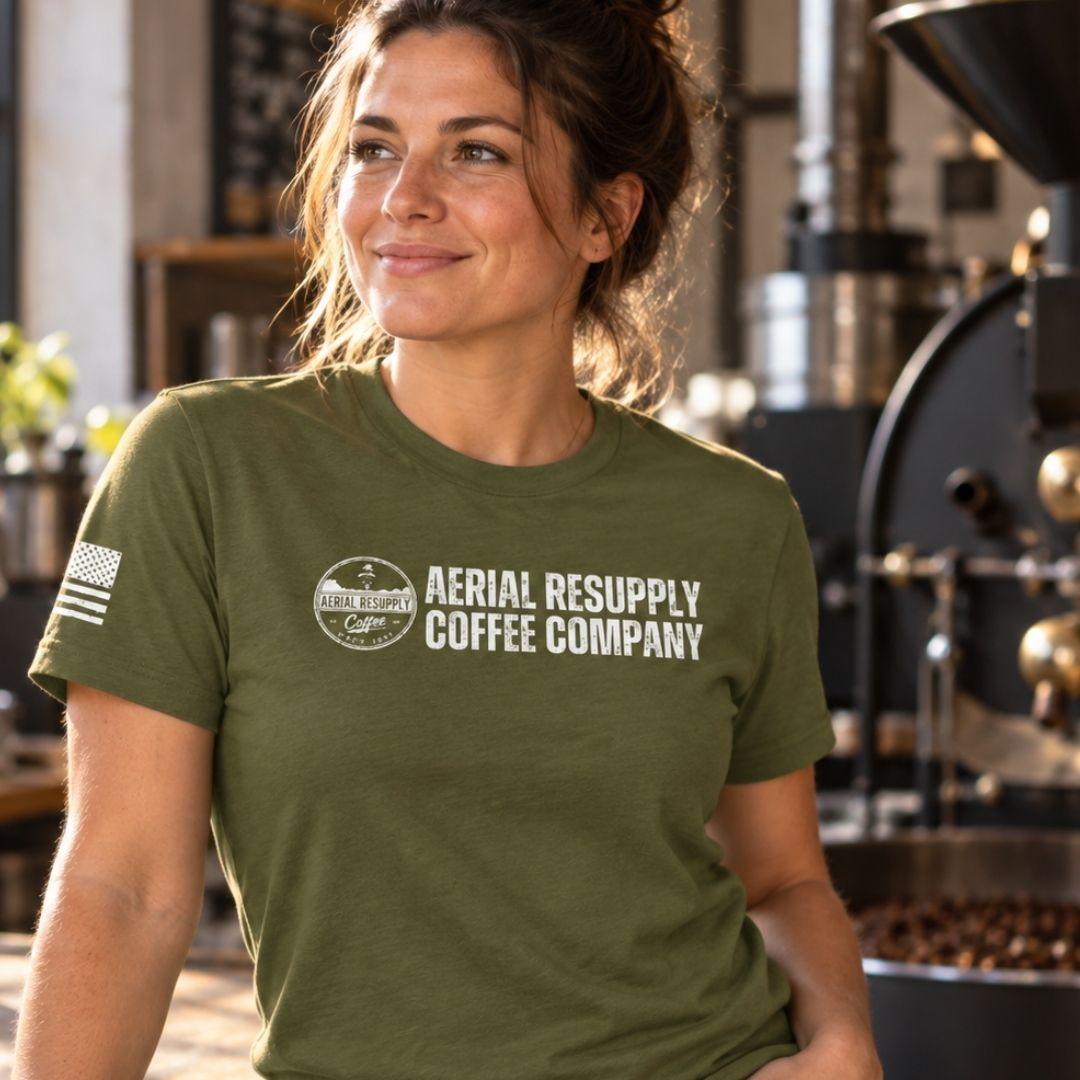 A woman wearing a green shirt in a roastery with the words aerial resupply coffee company on it
