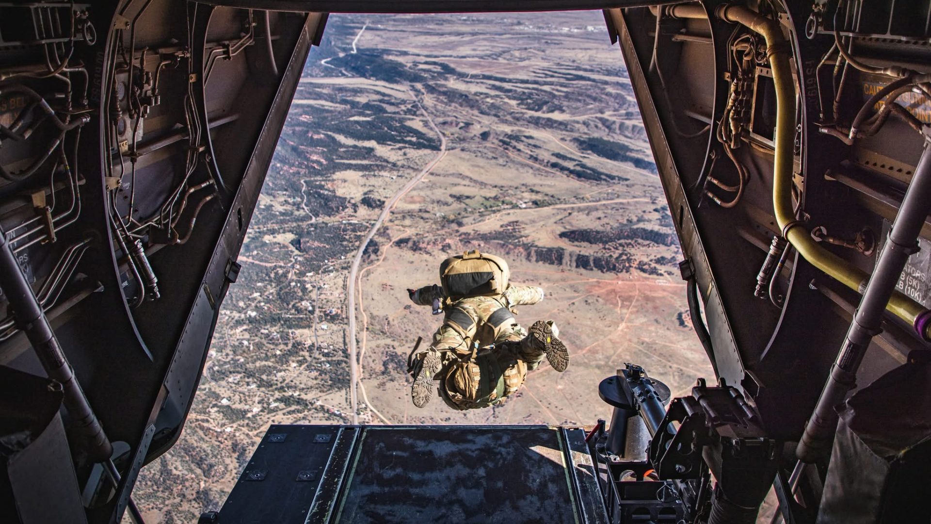 Person freefalling from an aircraft with a parachutist below, over a landscape.
