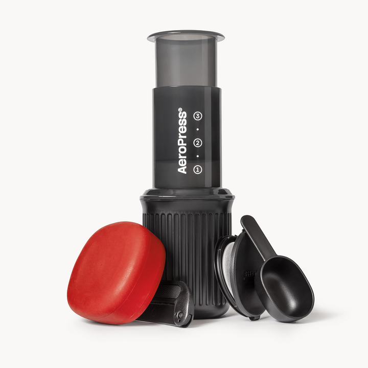 AeroPress Go coffee maker with its black mug, red silicone lid, scoop, stirrer and filter cap