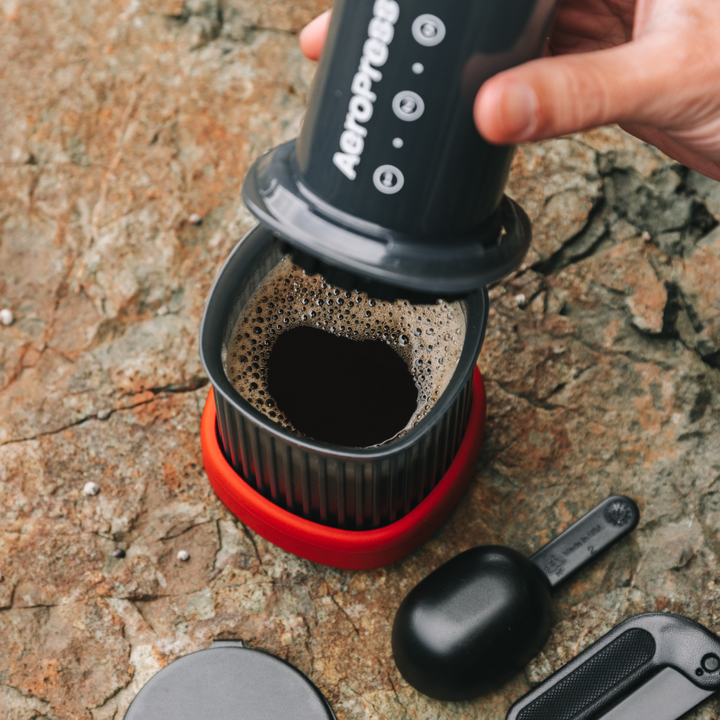 Pressing a fresh cup of coffee with the AeroPress Go on a rock outdoors