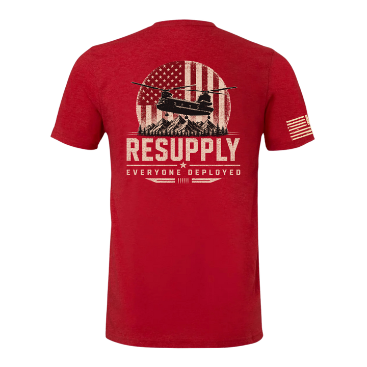 A red short-sleeve t-shirt shown from the back, featuring a distressed graphic of a military helicopter in front of an American flag and mountains, with the text 'RESUPPLY' and 'EVERYONE DEPLOYED'. A small American flag is printed on the left sleeve.