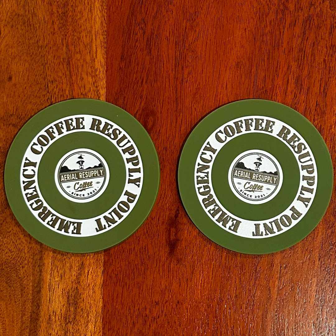 A logistics wins wars coffee mug and an Aerial Resupply Coffee emergency resupply coaster sitting on a table